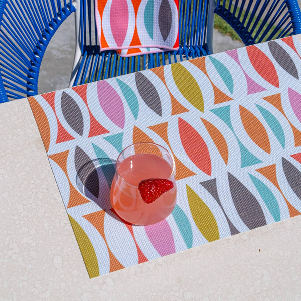 Colorful placemat with a drink on a table, next to a blue wicker chair.